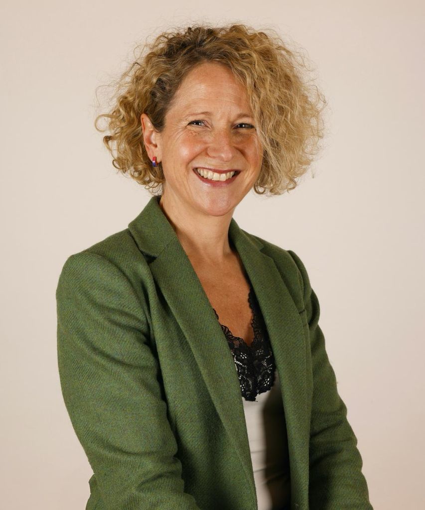 midlife woman with curly blonde hair smiling in a green blazer
