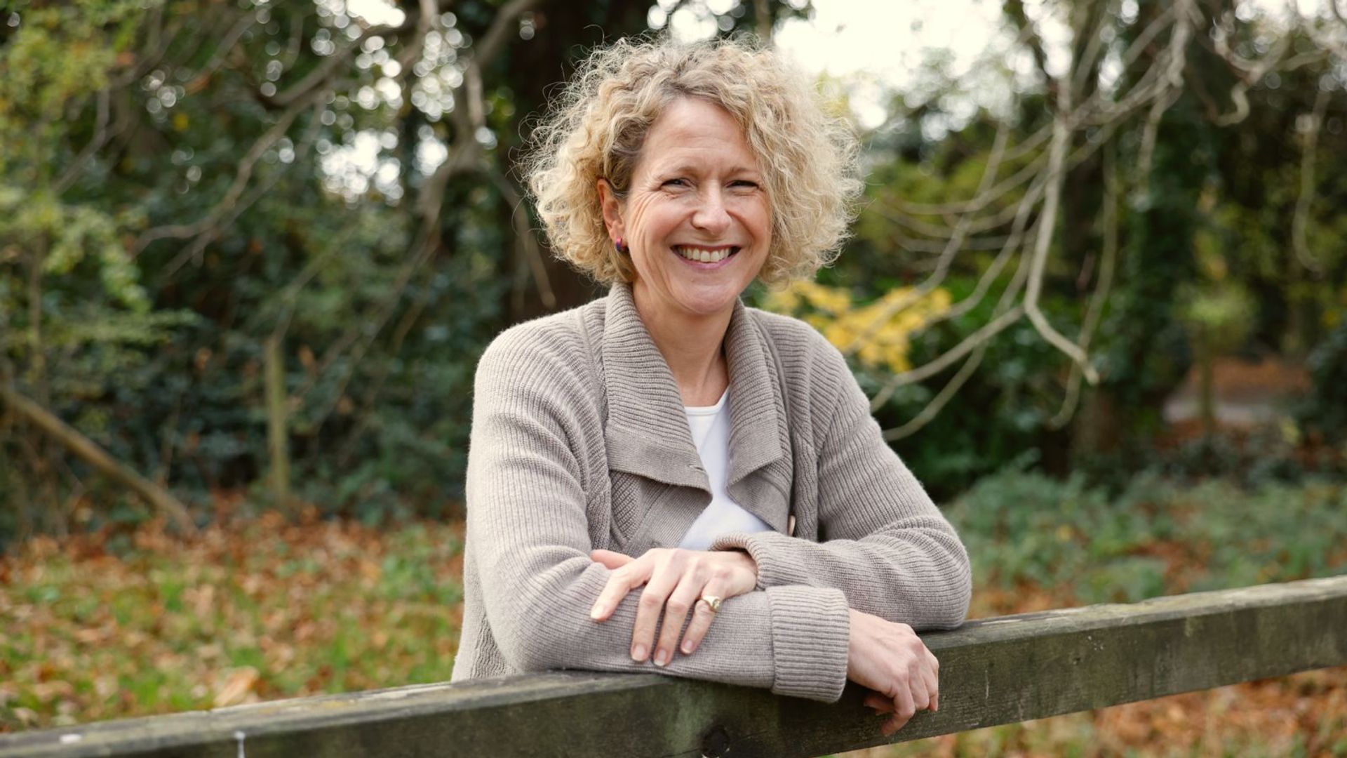 blonde woman with curly hair smiling and leaning on a gate